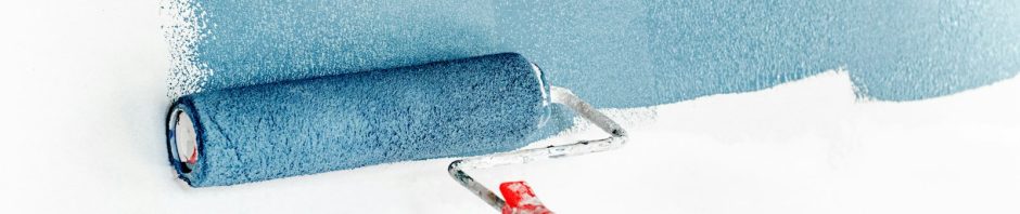 A paint roller spreading blue paint across a white wall